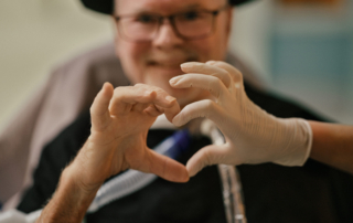 Patient with a Vocolair speaking valve and nurse using their hands to create a heart shape,
